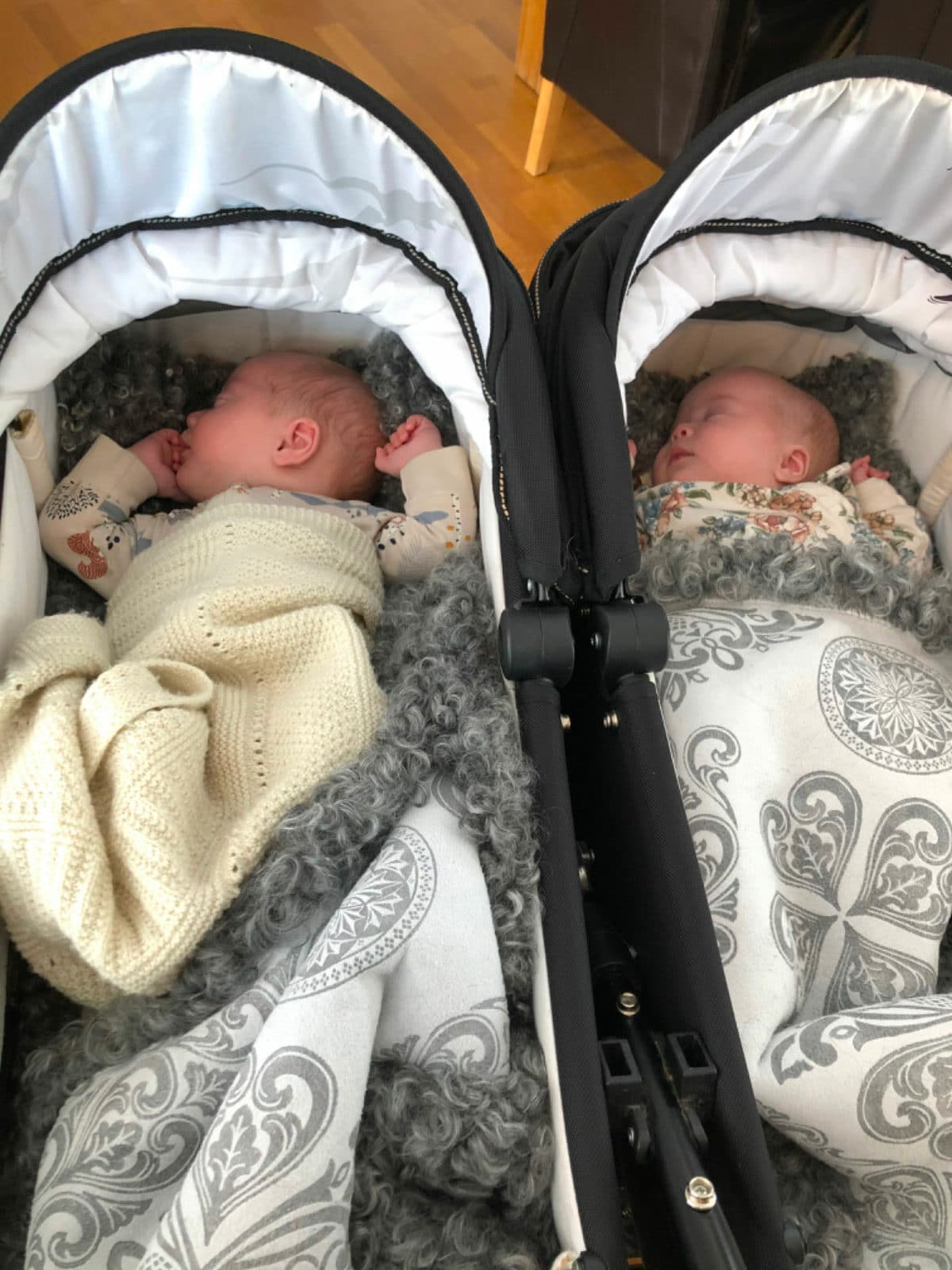 To babyer i tvillingvogn med babyposer av saueskinn.